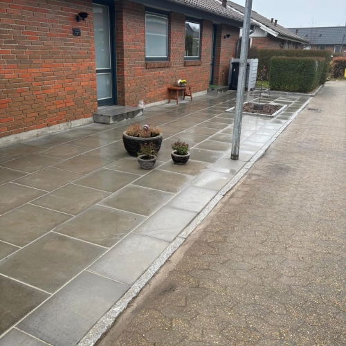 Belægning langs hus og fortov i Hurup nær Thisted med store lyse fliser og dekorative krukker