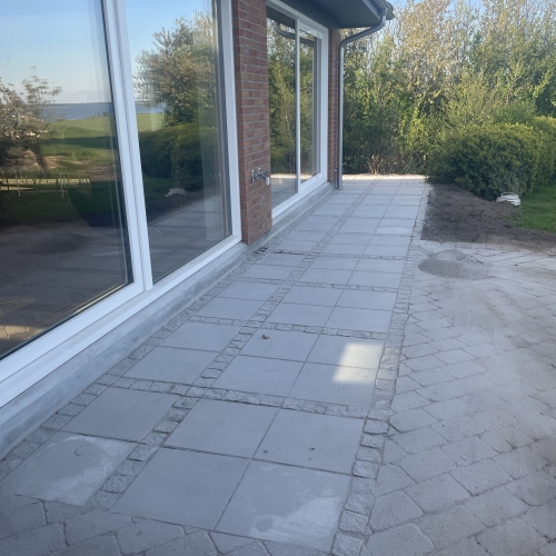 Belægning med lyse terrassefliser langs hus i Hurup nær Thisted med dekorativ kantafslutning